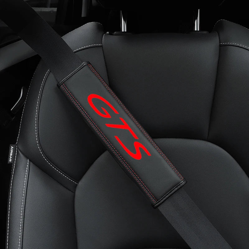 A close-up view of a black leather seat belt cover with red stitching and the GTS logo on a car seat.