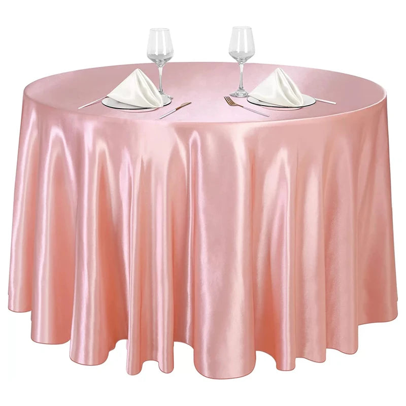 A round table set with a pink satin tablecloth, silverware, and wine glasses for an elegant event.