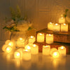 A collection of glowing white LED tea lights arranged on a wooden surface with a floral arrangement in the background.