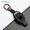 A slim carbon fiber car key cover with a metal loop and electronic features is shown on a dark surface.