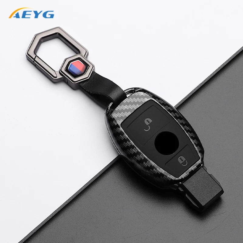 A slim carbon fiber car key cover with a metal loop and electronic features is shown on a dark surface.