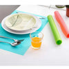 A set of colorful silicone mats and a glass are displayed on a white table.
