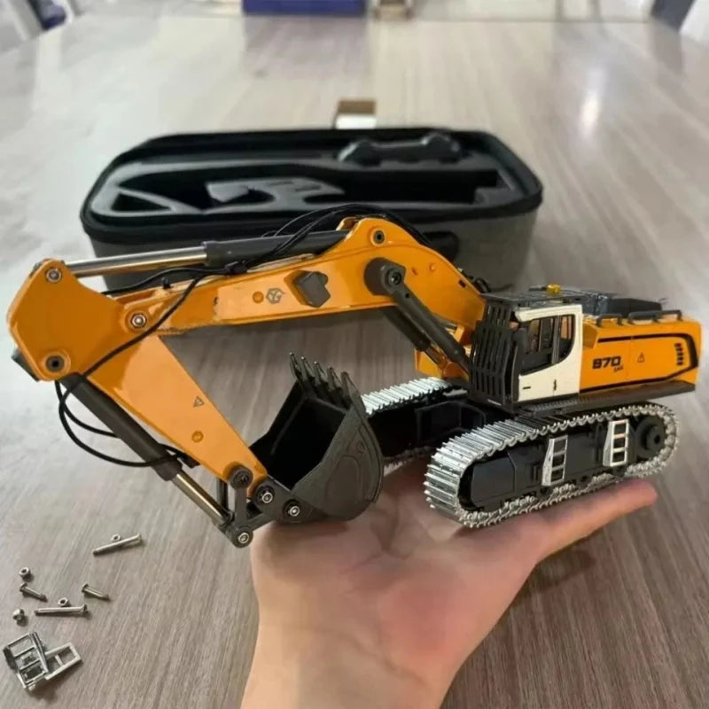 A hand holds a yellow and black 1:50 scale remote control excavator model with a digging attachment.
