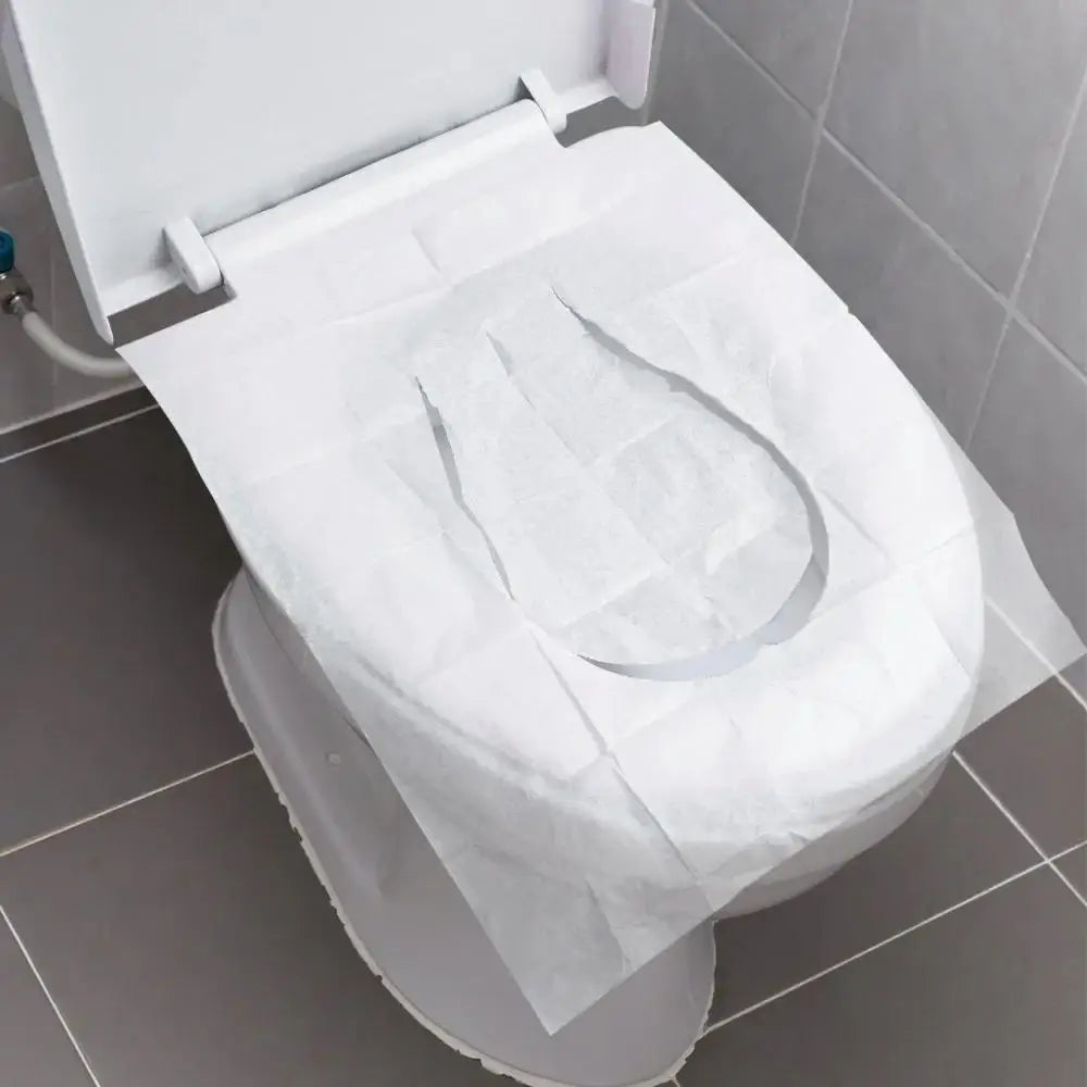 A white disposable toilet seat cover is placed on a toilet bowl in a bathroom setting.