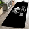 Black non-slip kitchen mat with white cutlery design on a light wooden floor.