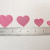 A row of five pink embroidered heart iron-on patches laid out next to a ruler.