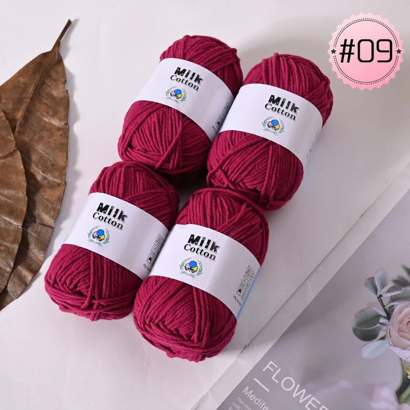 A stack of deep magenta milk cotton yarn skeins with white labels and a leaf in the background.