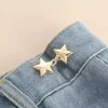 A close-up of a silver star brooch pinned onto blue denim fabric.