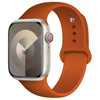 A silver Apple Watch is shown attached to a wide, orange silicone sport band.