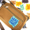 A tan canvas bag with a zippered pocket featuring embroidered humorous iron-on patches encouraging positivity and hard work.