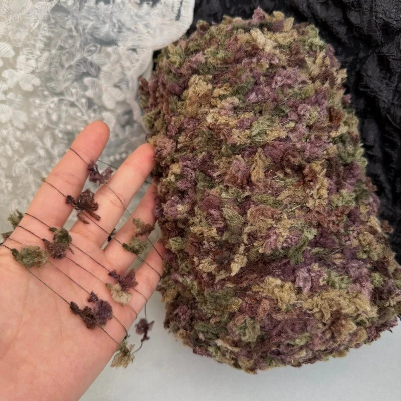 A ball of hand-dyed variegated yarn with purple and green tones resting on a hand.