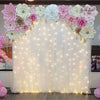 A white draped backdrop decorated with pink and cream floral arrangements and illuminated by fairy lights.