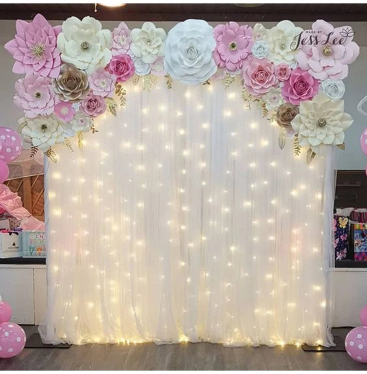 A white draped backdrop decorated with pink and cream floral arrangements and illuminated by fairy lights.