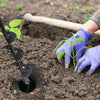 A hand wearing a purple glove is using a black garden auger to create a hole in dark soil for planting.