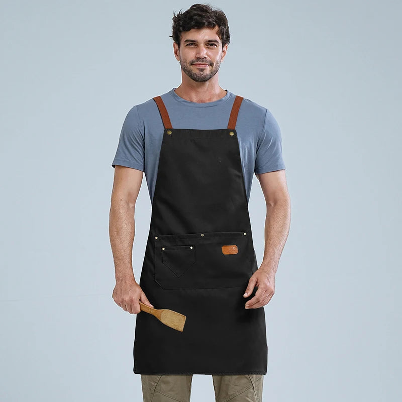 A man wearing a black waterproof adjustable kitchen apron over a gray t-shirt.