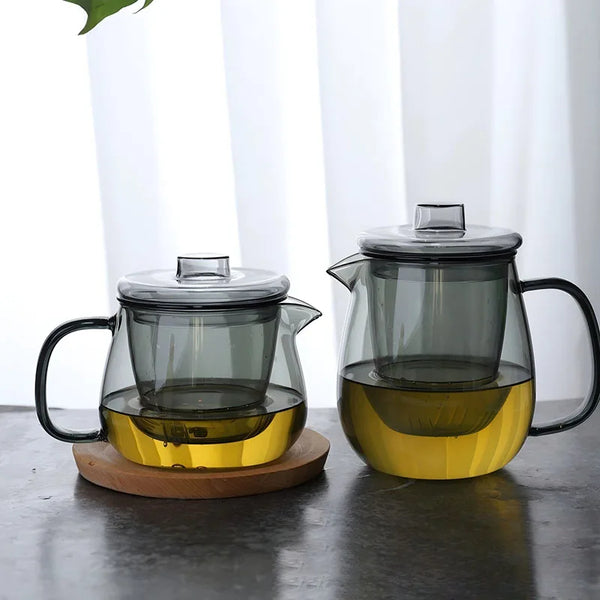 A clear glass teapot with a removable infuser filled with golden-yellow tea on a wooden coaster.
