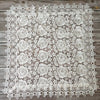 White lace tablecloth featuring an embroidered rose pattern on a rustic wooden surface.