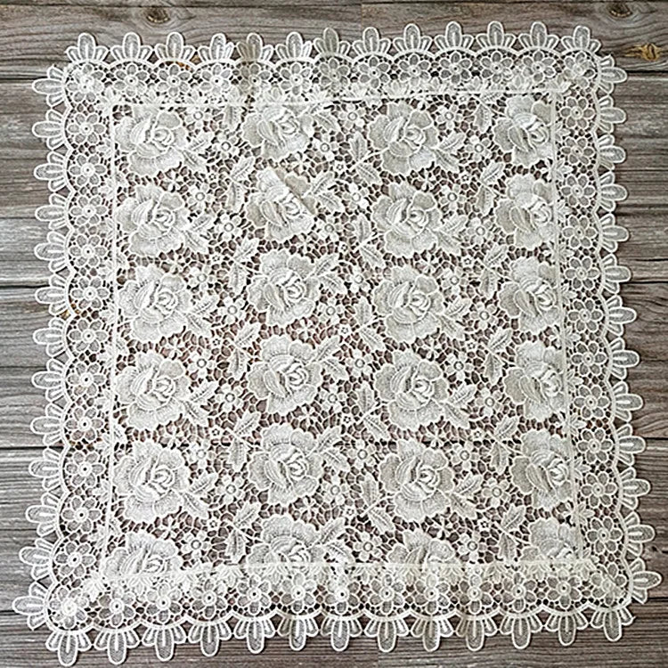 White lace tablecloth featuring an embroidered rose pattern on a rustic wooden surface.