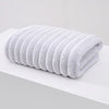 A stack of white plush coral velvet bath towels rolled neatly on a white surface.