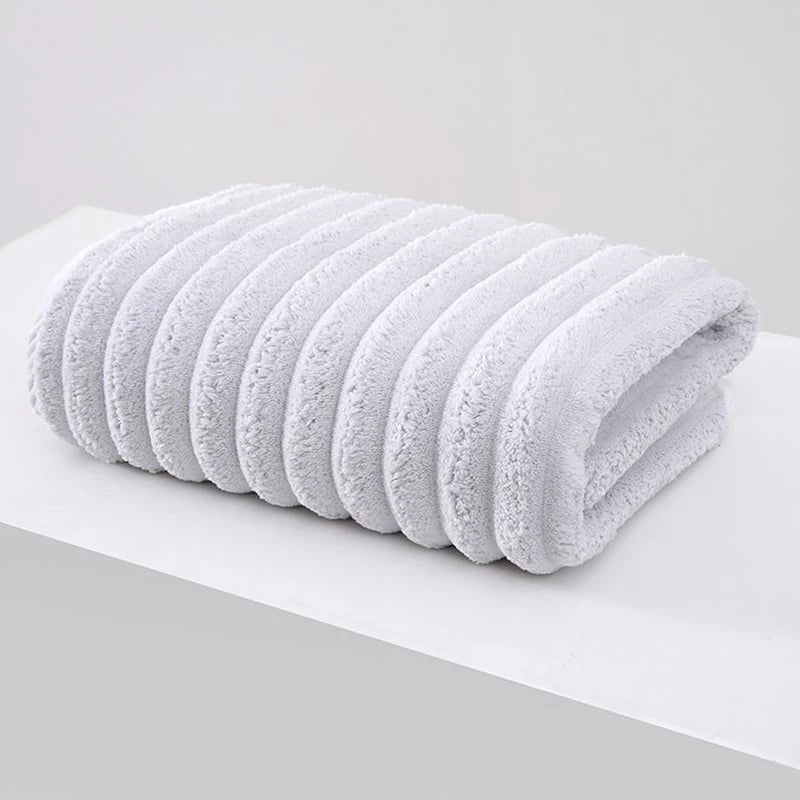 A stack of white plush coral velvet bath towels rolled neatly on a white surface.