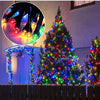 A decorated Christmas tree illuminated with colorful LED string lights in an outdoor garden setting.