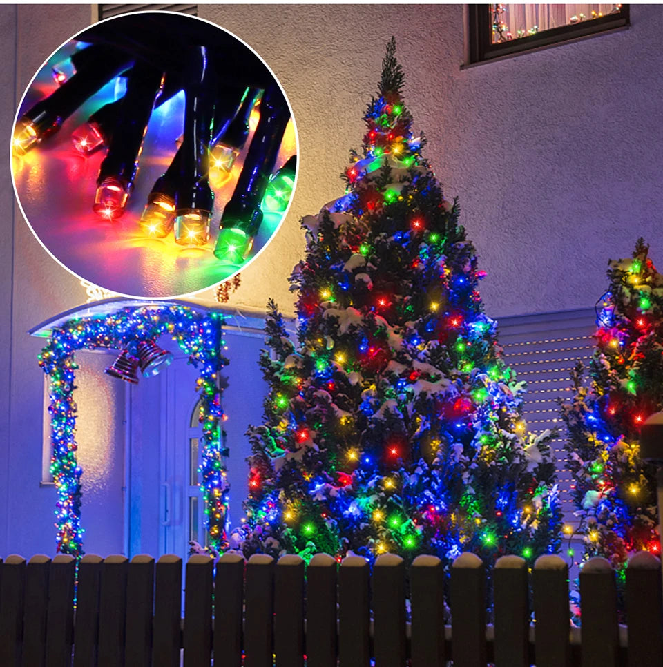 A decorated Christmas tree illuminated with colorful LED string lights in an outdoor garden setting.