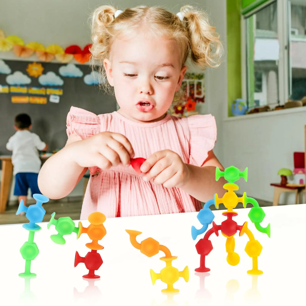 A young girl is playing with colorful silicone suction bath toys on a white table.