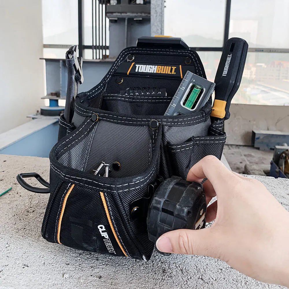 A black heavy-duty construction tool pouch with a cliptech hub and hammer loop is held by a hand.
