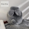A deep grey plush rabbit hot water bottle with a soft flannel cover resting on a textured gray surface.