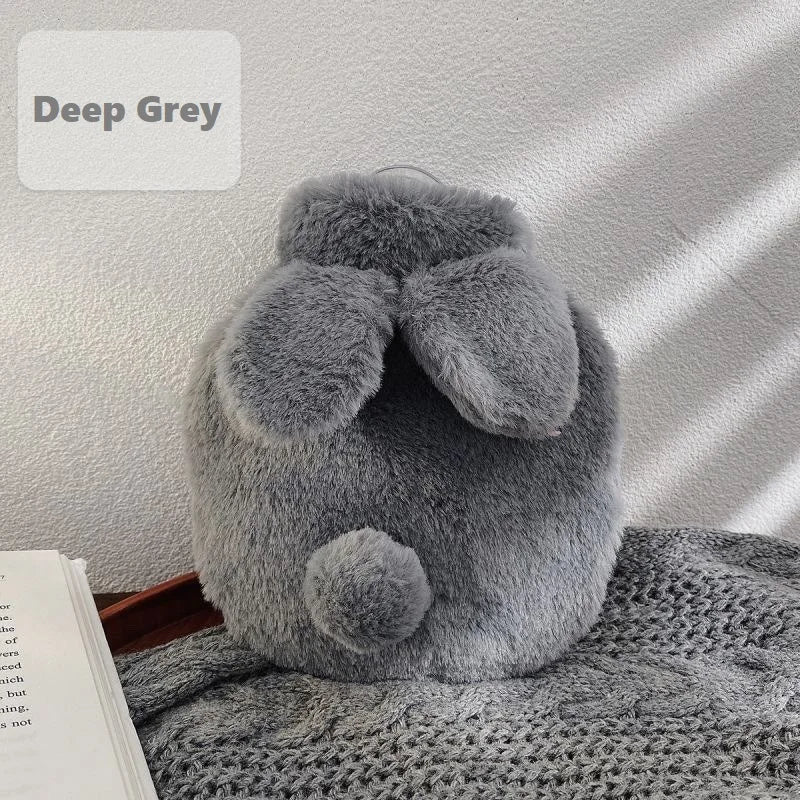 A deep grey plush rabbit hot water bottle with a soft flannel cover resting on a textured gray surface.