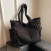 A black women's corduroy tote bag with an adjustable strap resting on a dark surface.