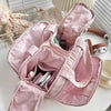 A pink travel makeup bag with a wide opening is shown on a white surface.