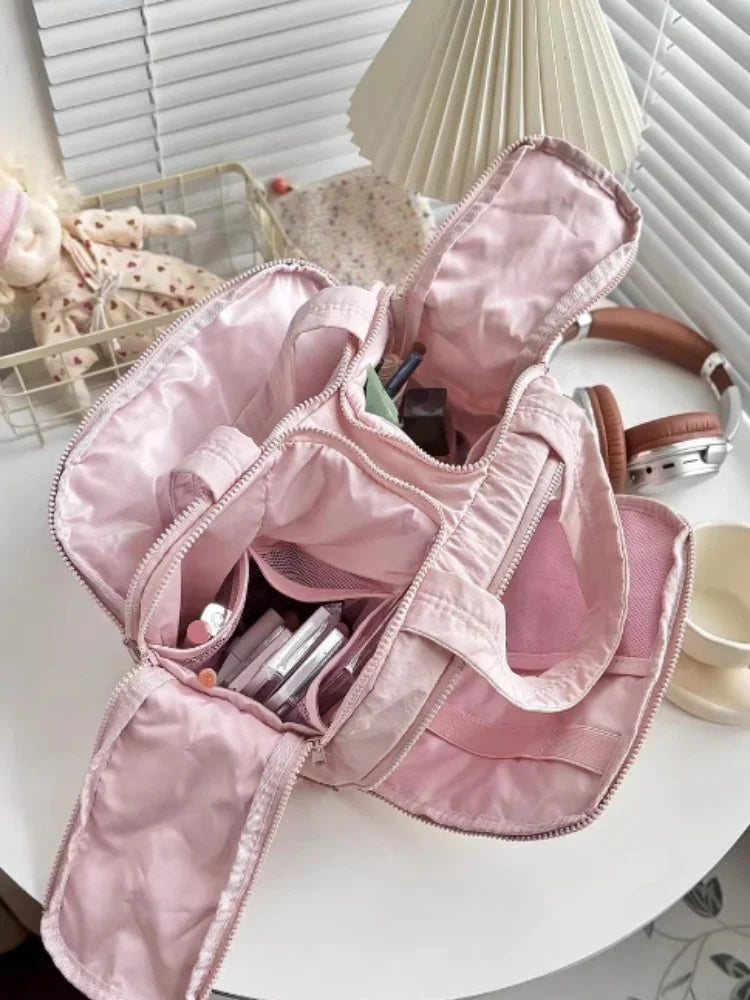 A pink travel makeup bag with a wide opening is shown on a white surface.