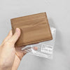 A hand holds a brown genuine leather slim card holder wallet packaged in clear plastic.