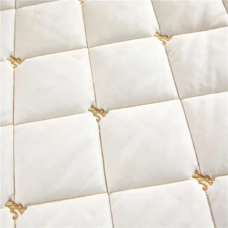 White quilted bed skirt with gold embroidery on a diamond pattern.