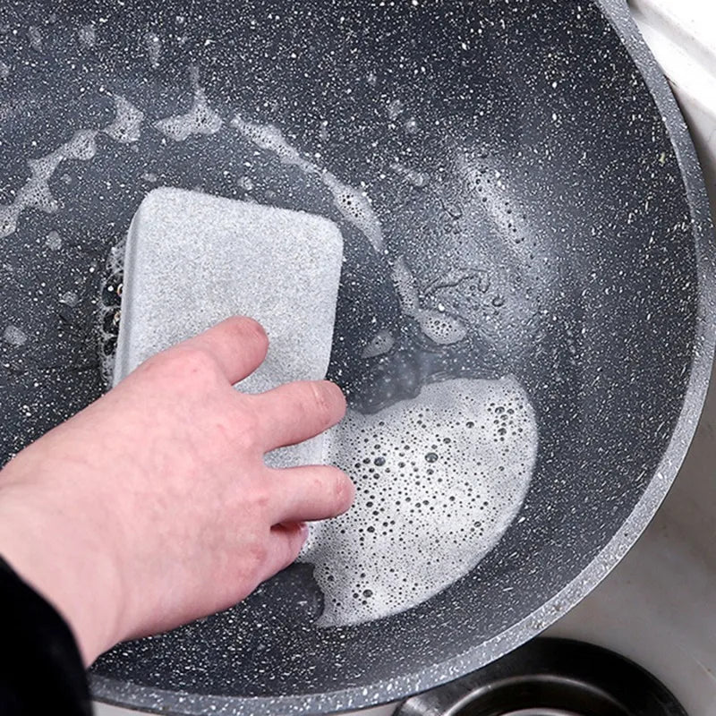 A hand is placing a gray cleaning sponge into a dark gray, speckled dish or bowl.