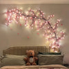 A decorative cherry blossom tree lamp with pink LED lights mounted on a wall above a bed.