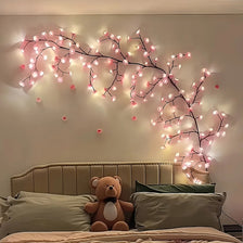 A decorative cherry blossom tree lamp with pink LED lights mounted on a wall above a bed.