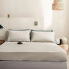A bed with a beige fitted sheet and pillows in a bright room.