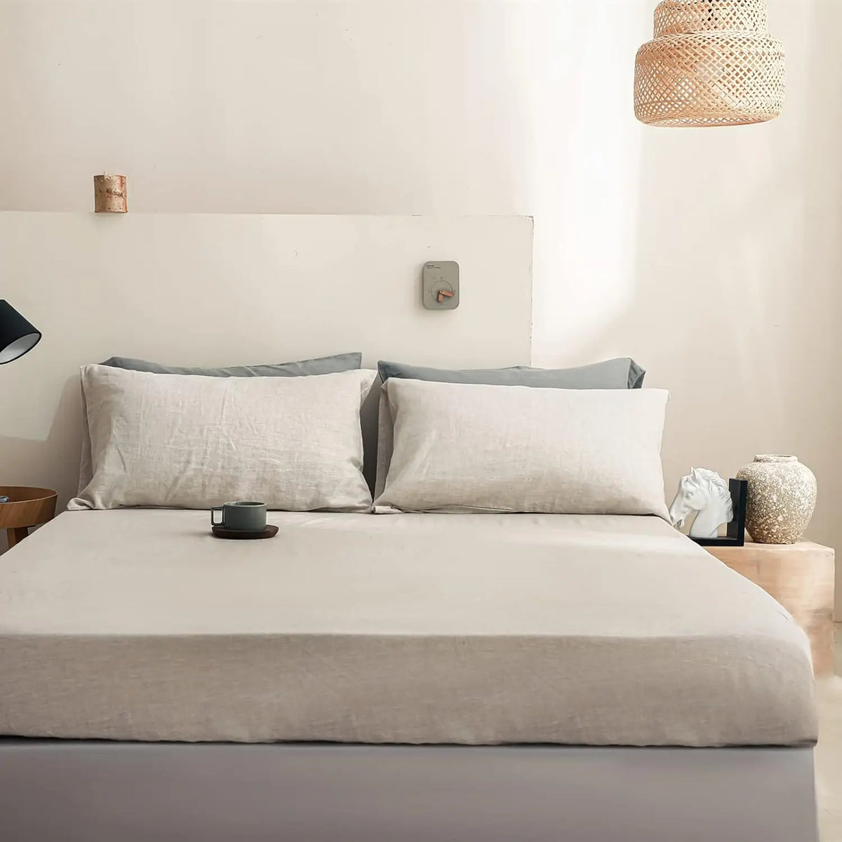 A bed with a beige fitted sheet and pillows in a bright room.