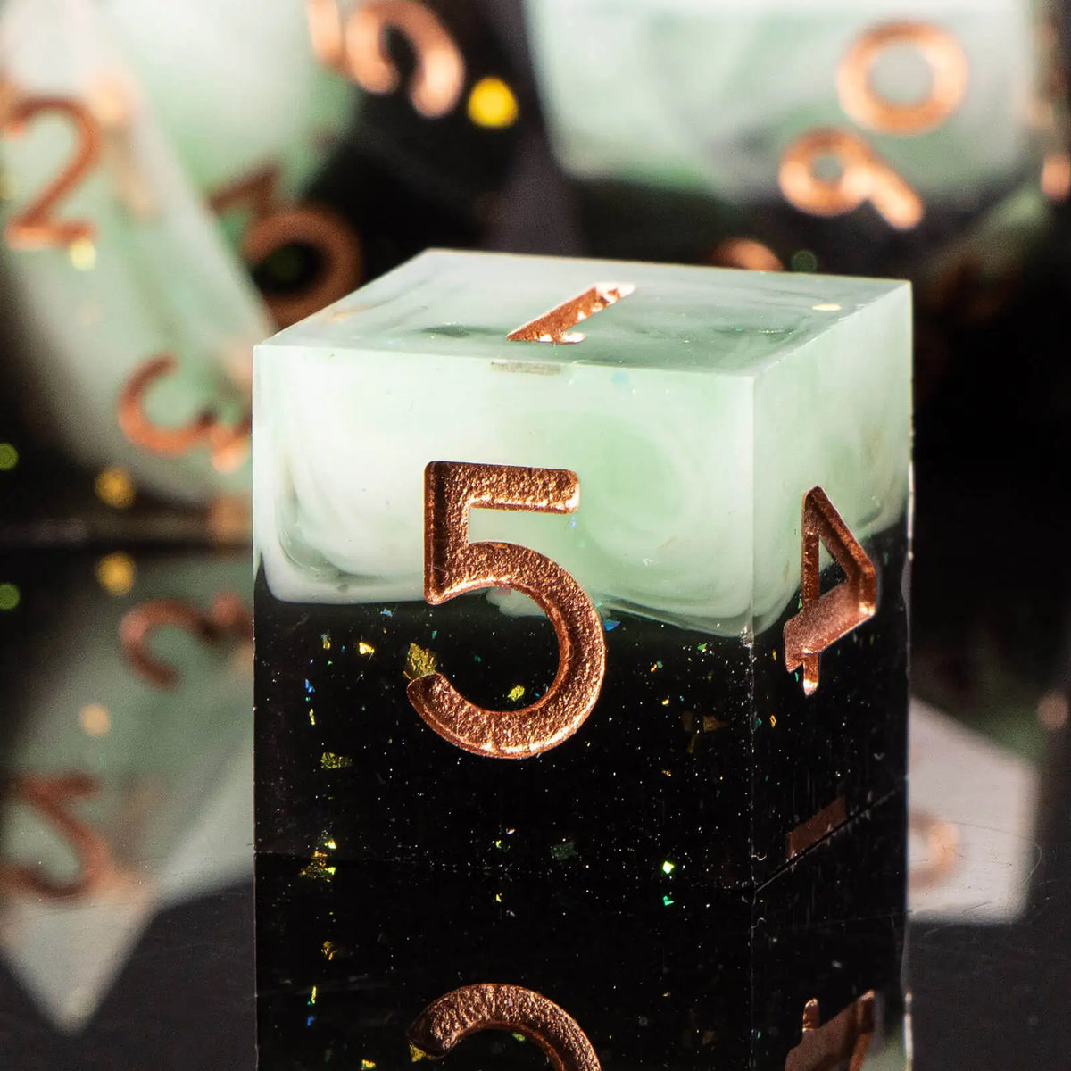 A clear green resin polyhedral die with the number 5 is shown on a dark surface.