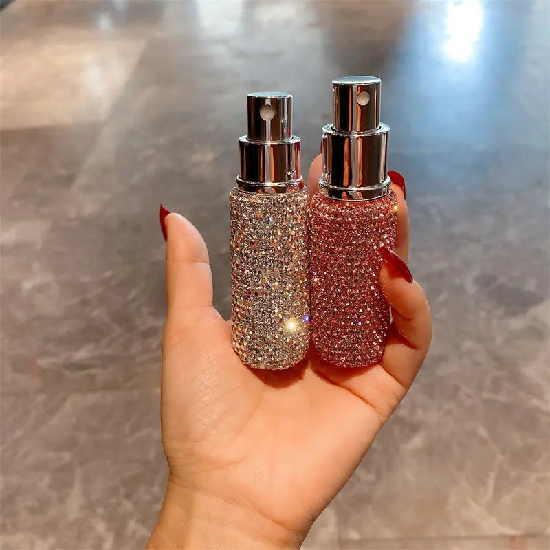 A hand holds a pink glitter perfume bottle with a silver atomizer and a matching glass bottle.