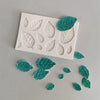 White silicone mold with embossed rose leaves and several green silicone rose leaves scattered nearby.