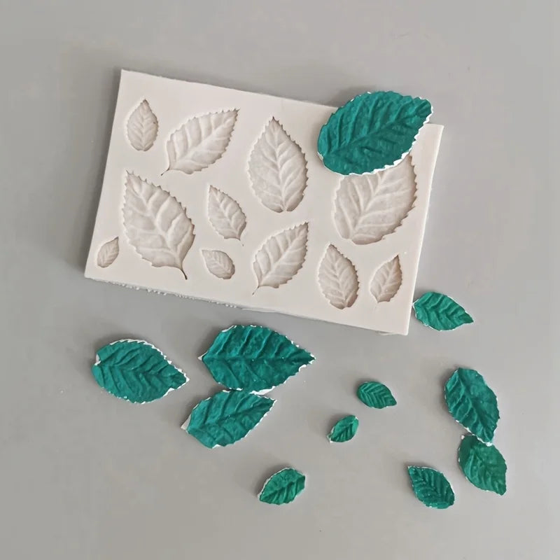 White silicone mold with embossed rose leaves and several green silicone rose leaves scattered nearby.