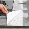 A hand applies a white self-adhesive marble effect peel-and-stick wallpaper onto a gray marble surface.