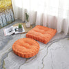 An orange thick corduroy floor cushion is placed on a light gray patterned floor near a window.