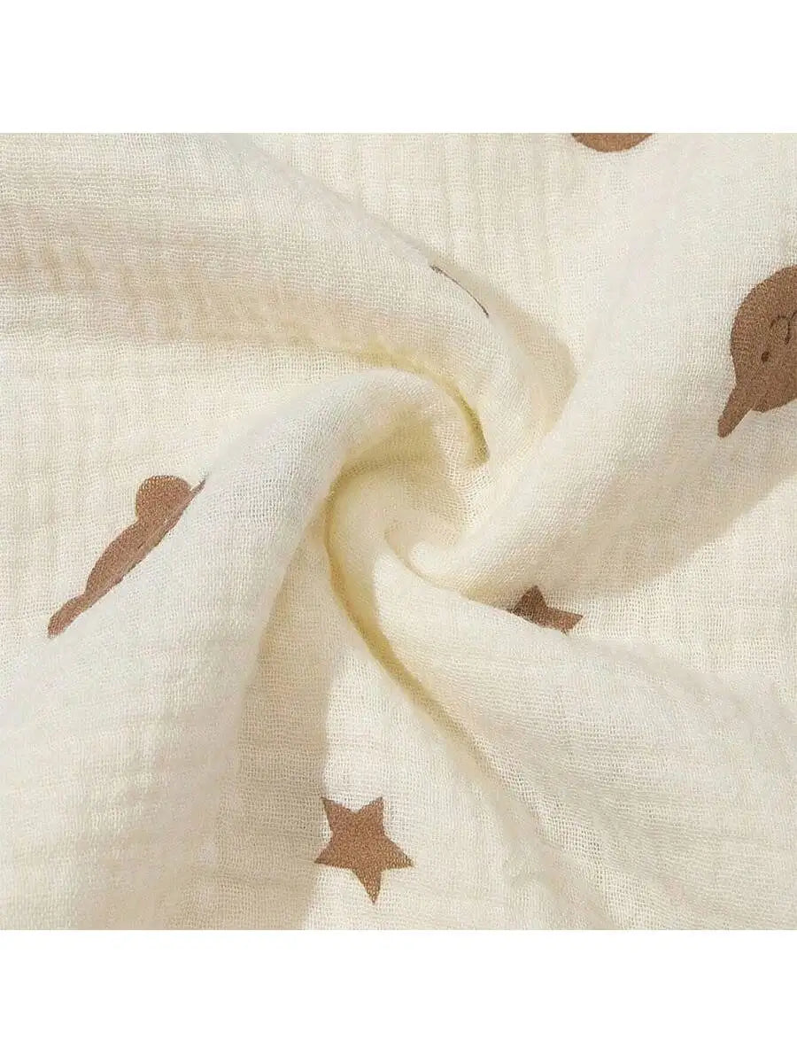 Close-up of a cream-colored fabric with small brown sun and dust motifs, showing the soft texture and drape.