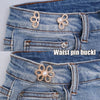 Close-up of a denim jean waistband featuring decorative gold and pearl waist pin buckles.