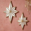 A pair of geometric star-shaped resin wall mirrors with gold trim mounted on a pink textured wall.