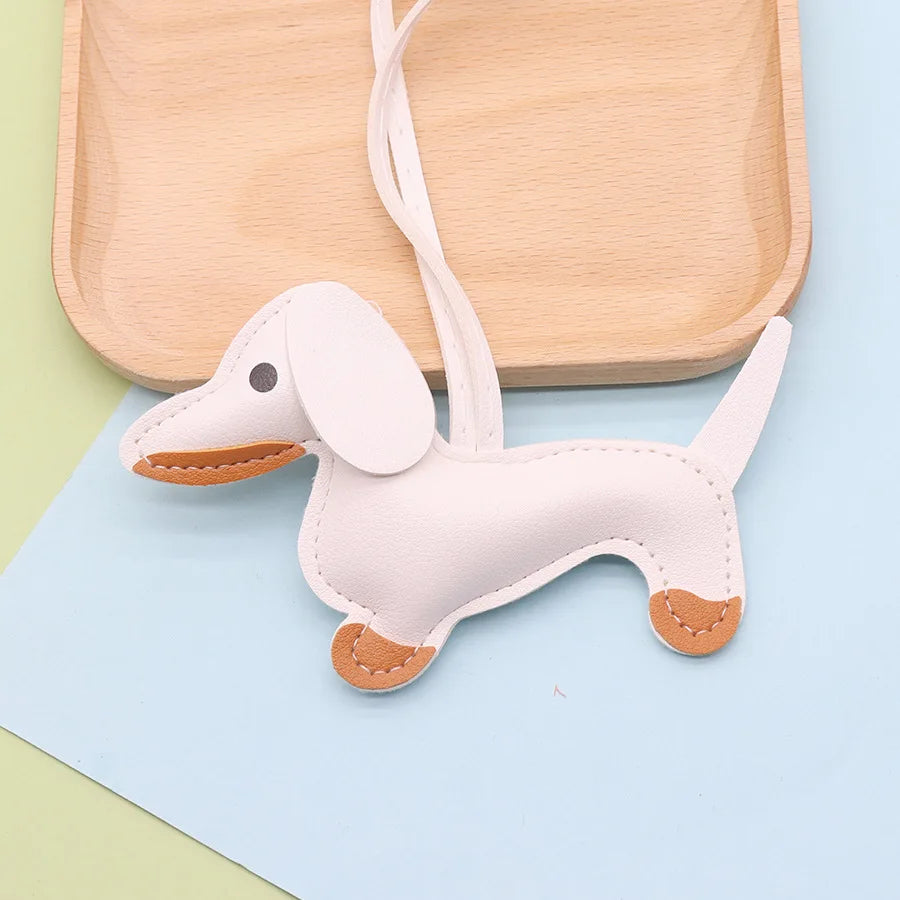 A light pink dachshund puppy keychain with tan accents resting on a wooden tray and blue paper.